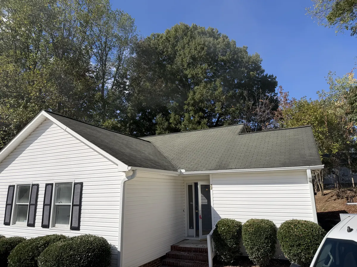 A white vinyl-sided home with an aging asphalt shingle roof treated by Roof Armor